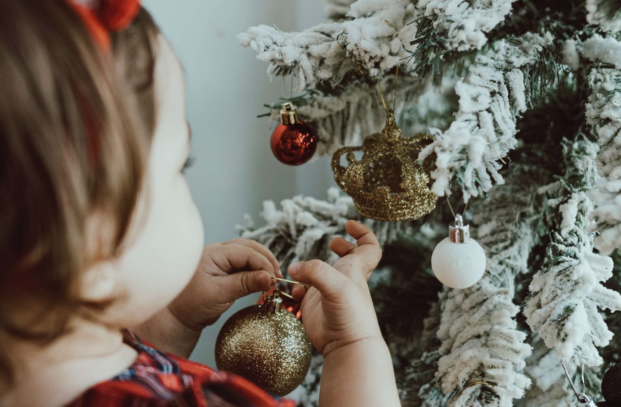 A baby girl is decorating a Christmas tree