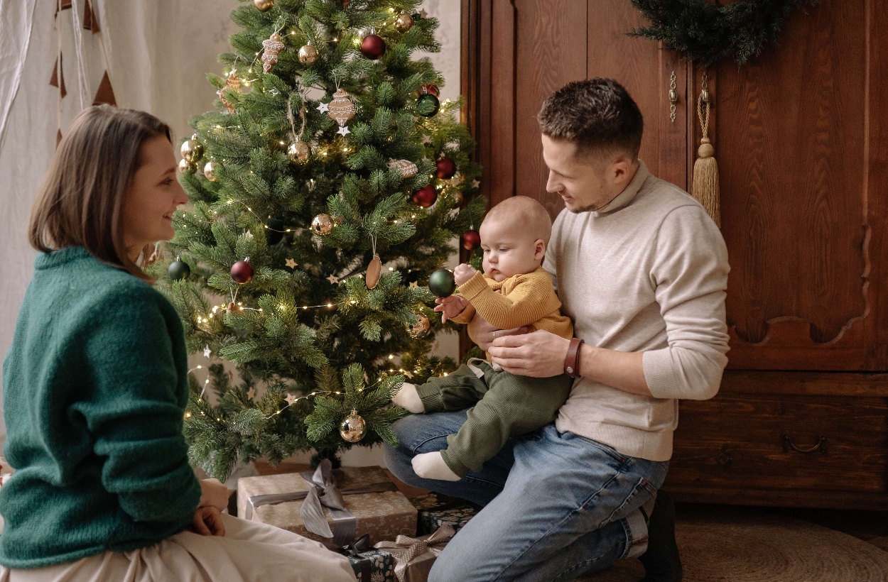 A baby is touching Christmas tree with its young parents