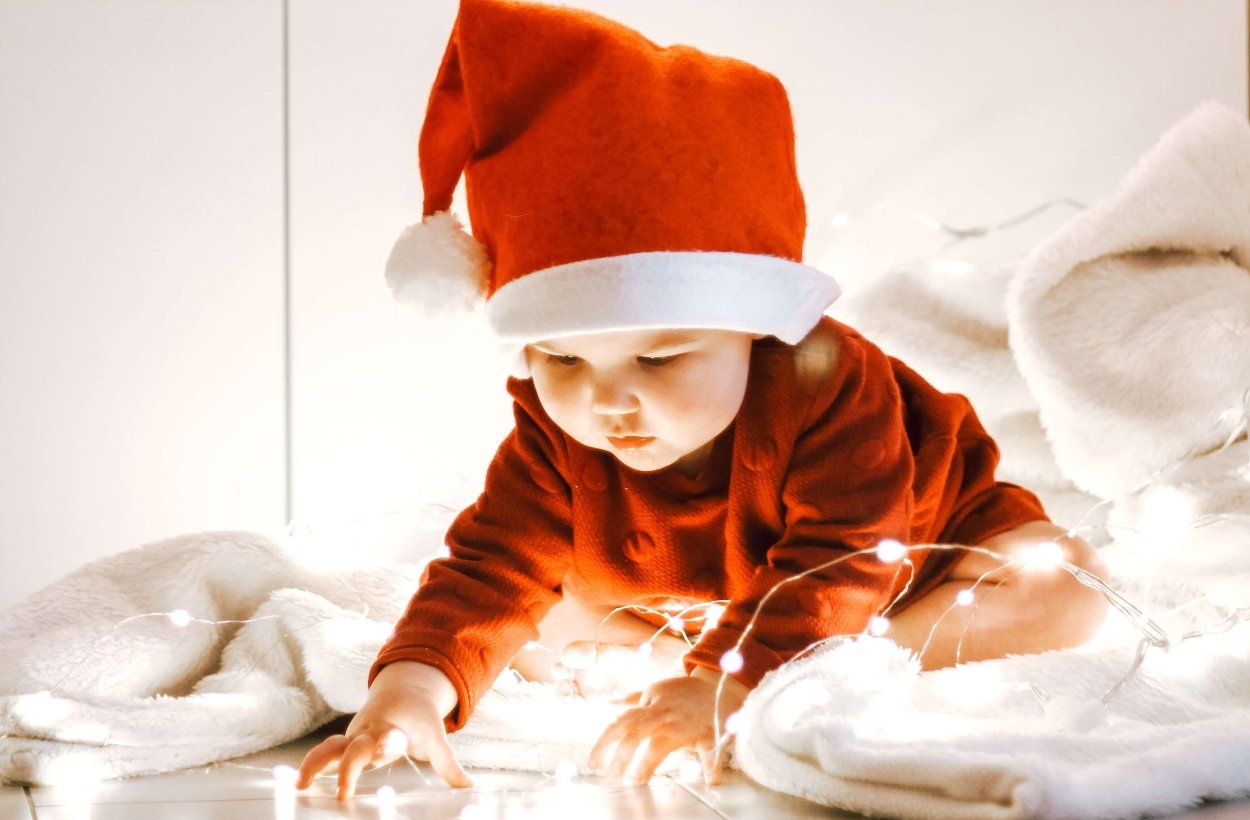 A baby wearing a Santa hat playing with Christmas lights