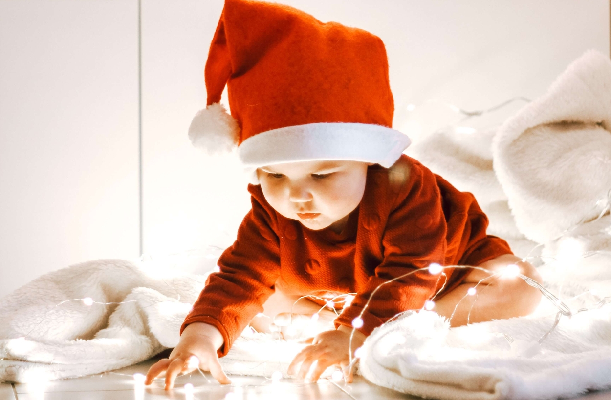 A baby wearing a Santa hat playing with Christmas lights