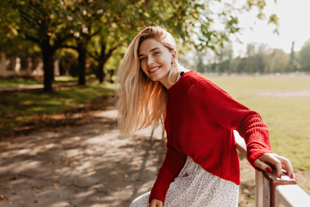 A beautiful girl in a red sweater leans on the railing in the park
