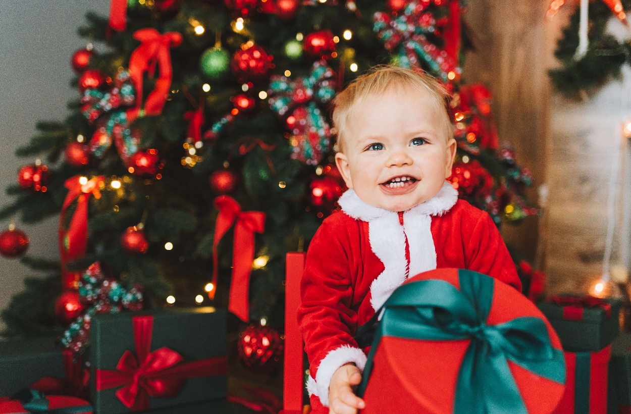 A cute baby holding a gift box in front of the Christmas tree