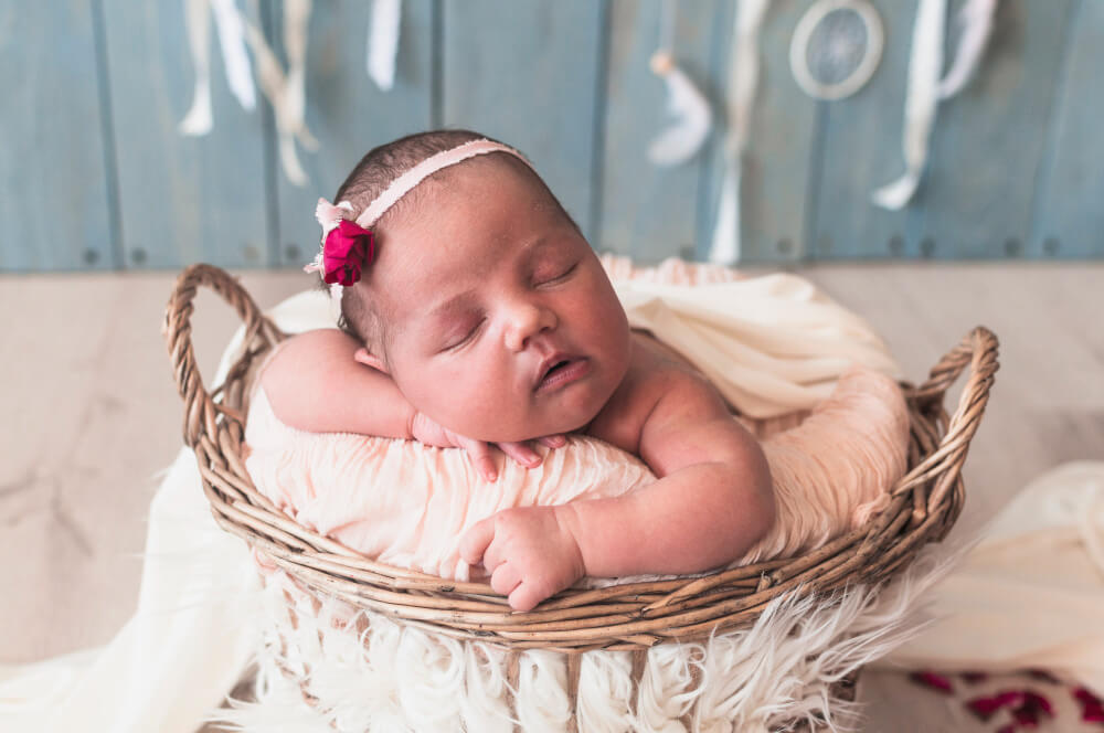 A cute newborn baby wearing a headgear sleeping in a basket