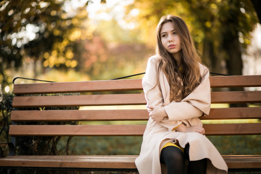 A girl in a windbreaker sits on a bench outdoors