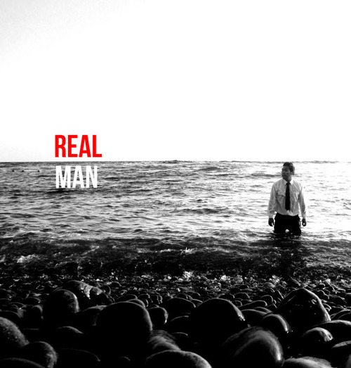 A man kneeling in the sea with REAL MAN text overhead