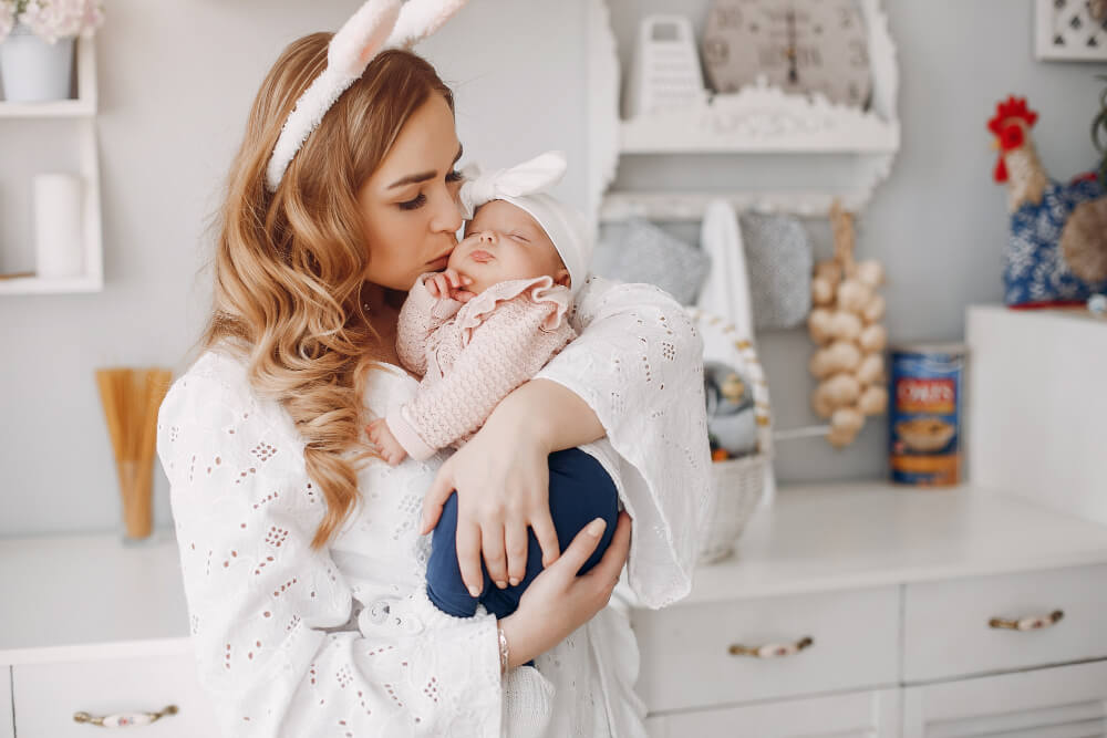 A mother with bunny ear accessories is kissing her newborn baby