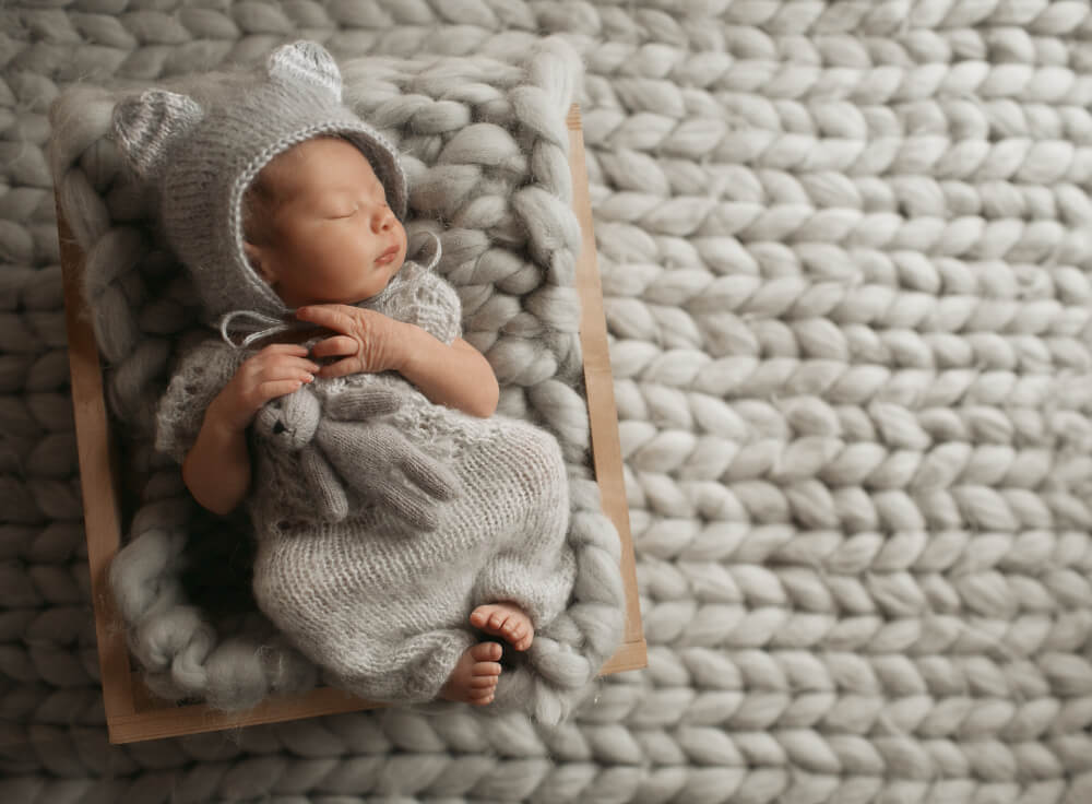 A newborn baby in a gray sweater is sleeping