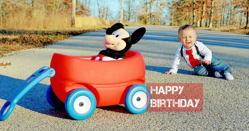 A toddler next to a toy wagon and a plush toy with HAPPY BIRTHDAY text on it