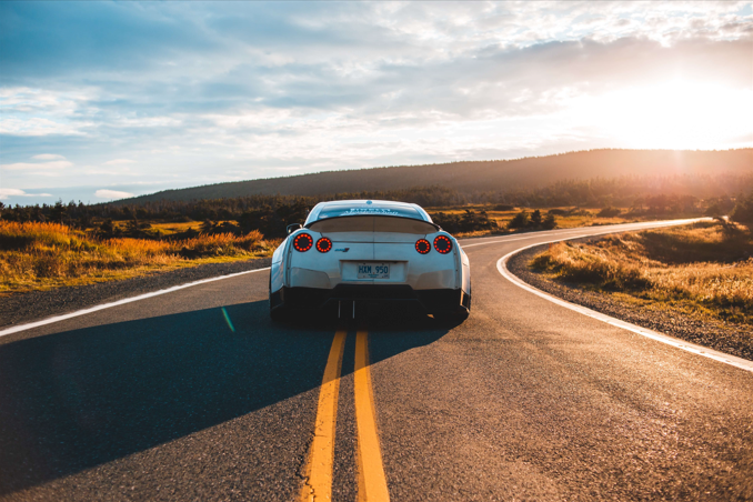 A white car is driving on a sunny road