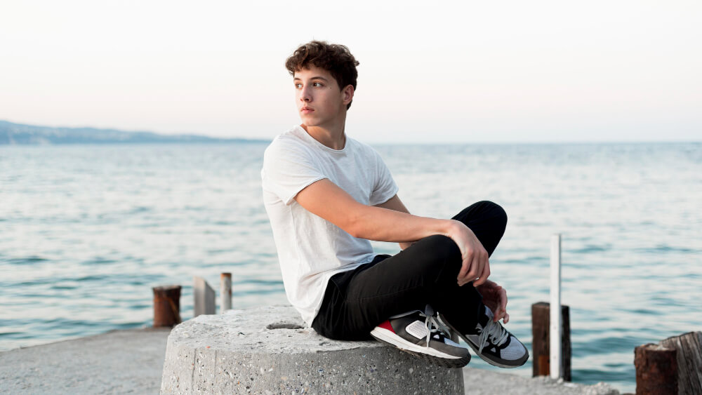 A young handsome boy sits by the sea
