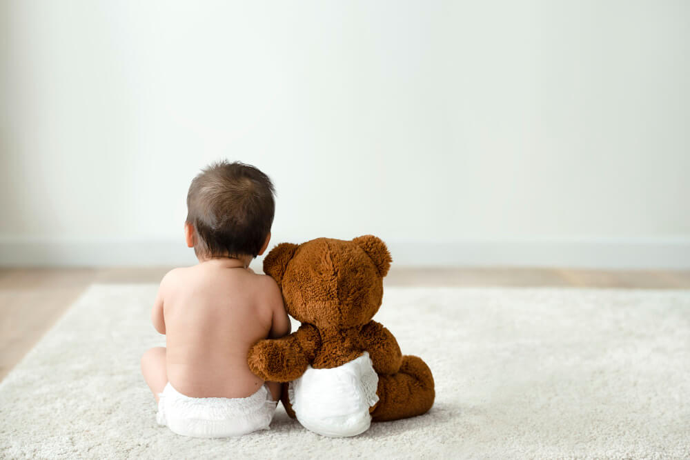 Back view of a newborn baby and a bear toy