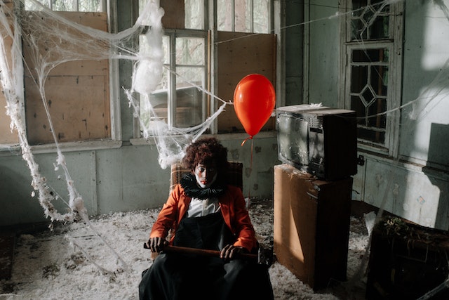 A man with an orange balloon sits in a shabby room
