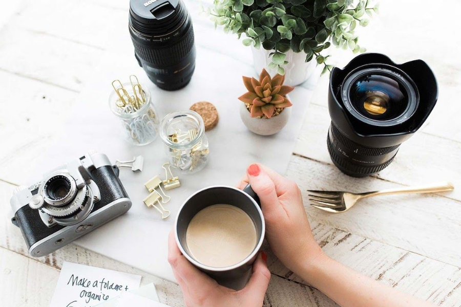 a black camera and lenses with a cup of coffe held by hands