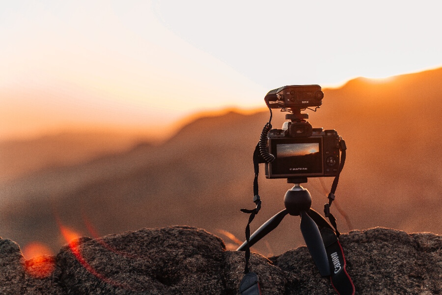 a black camera with a tripod and a red sky