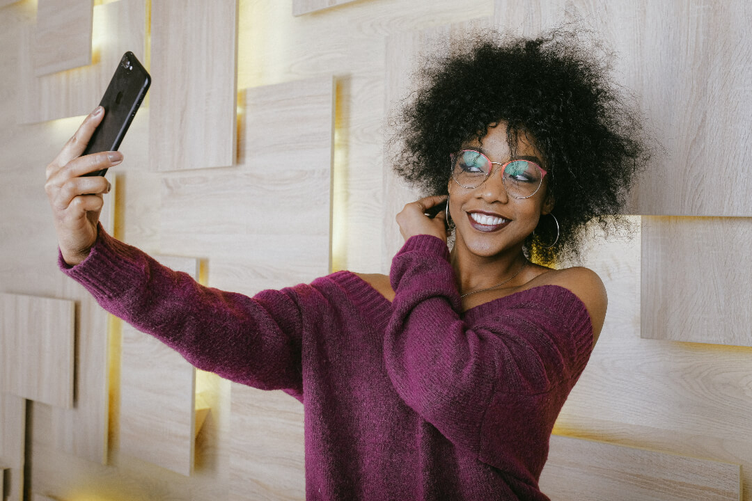 a black girl in glasses taking selfie near wall