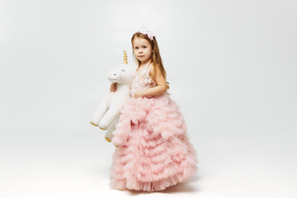 a litttle girl wearing pink princess dress and holding a unicorn doll