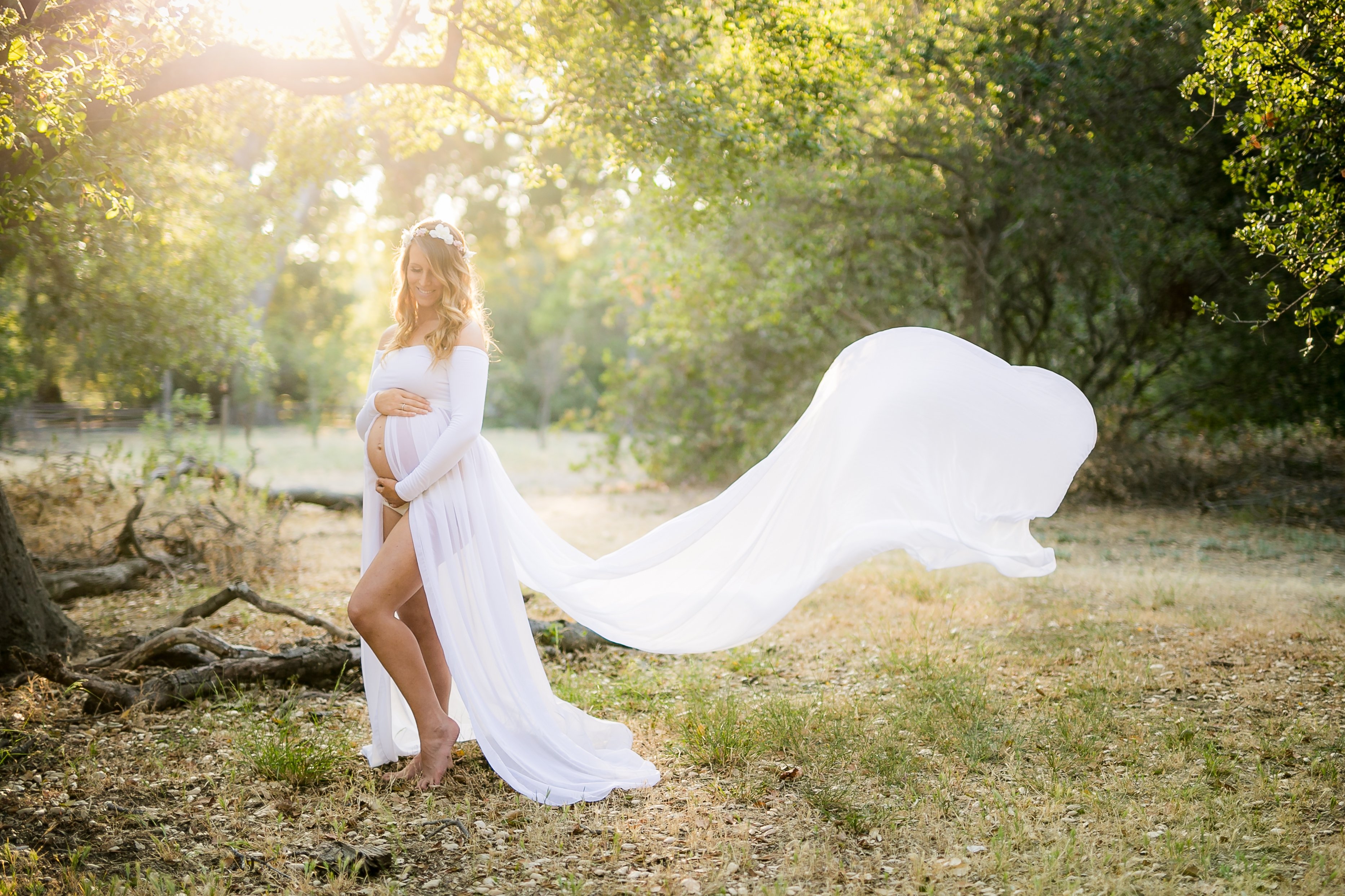 a pregnant female in white dress stands in the forest