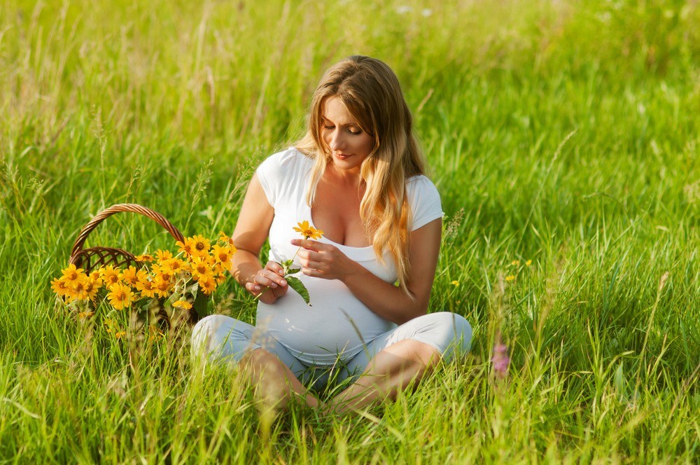 a pregnant woman on the grass with a daisy