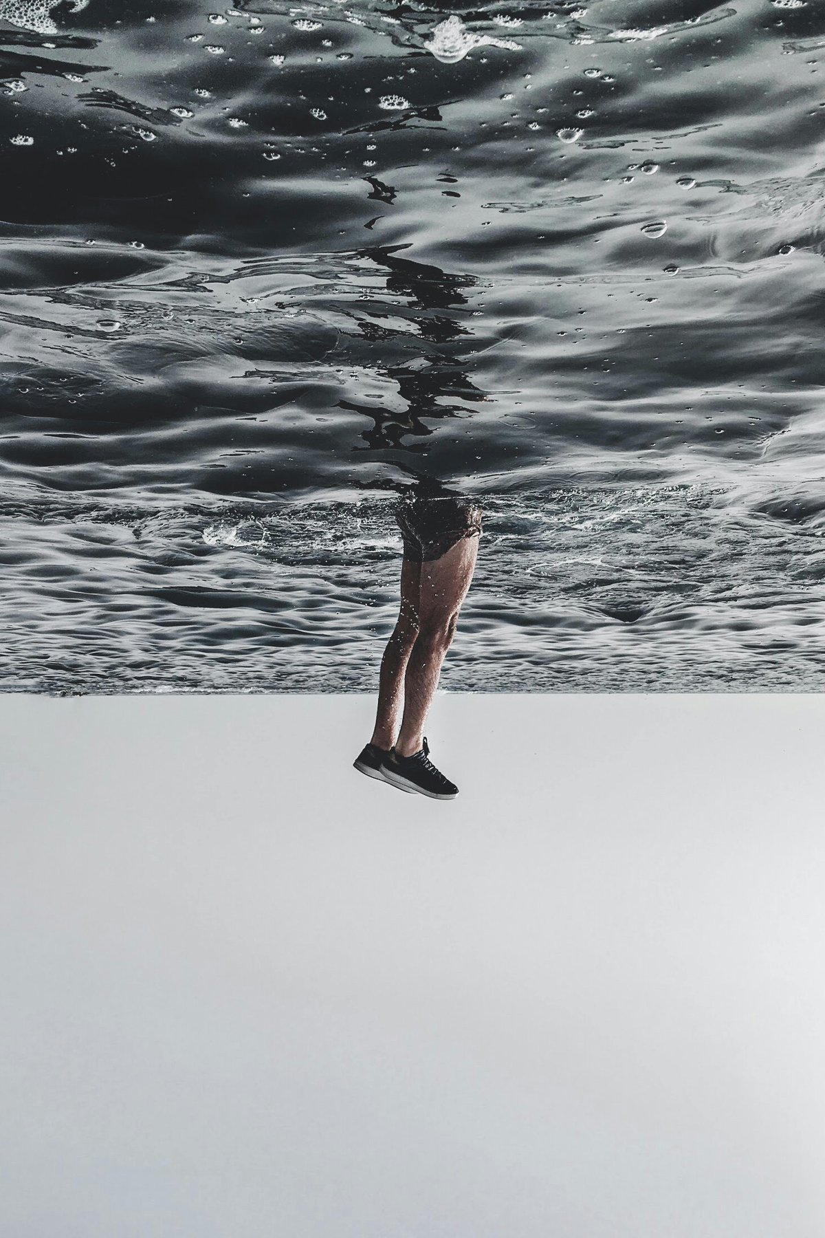 a surreal scene with water surface in the upper part and a person's body suspended upside down in the lower part