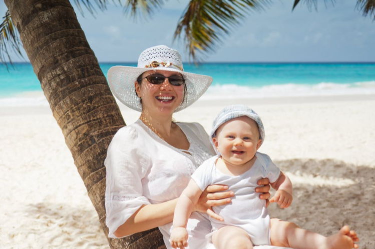 a woman and a baby is smiling at the camera on the beach