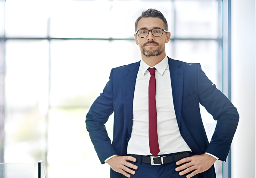 A man in suit-and-tie puts hands at hips and look directly to the camera