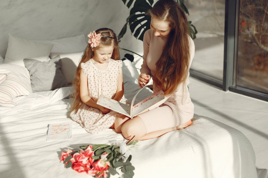 a female and her daughter reading books together on the bed