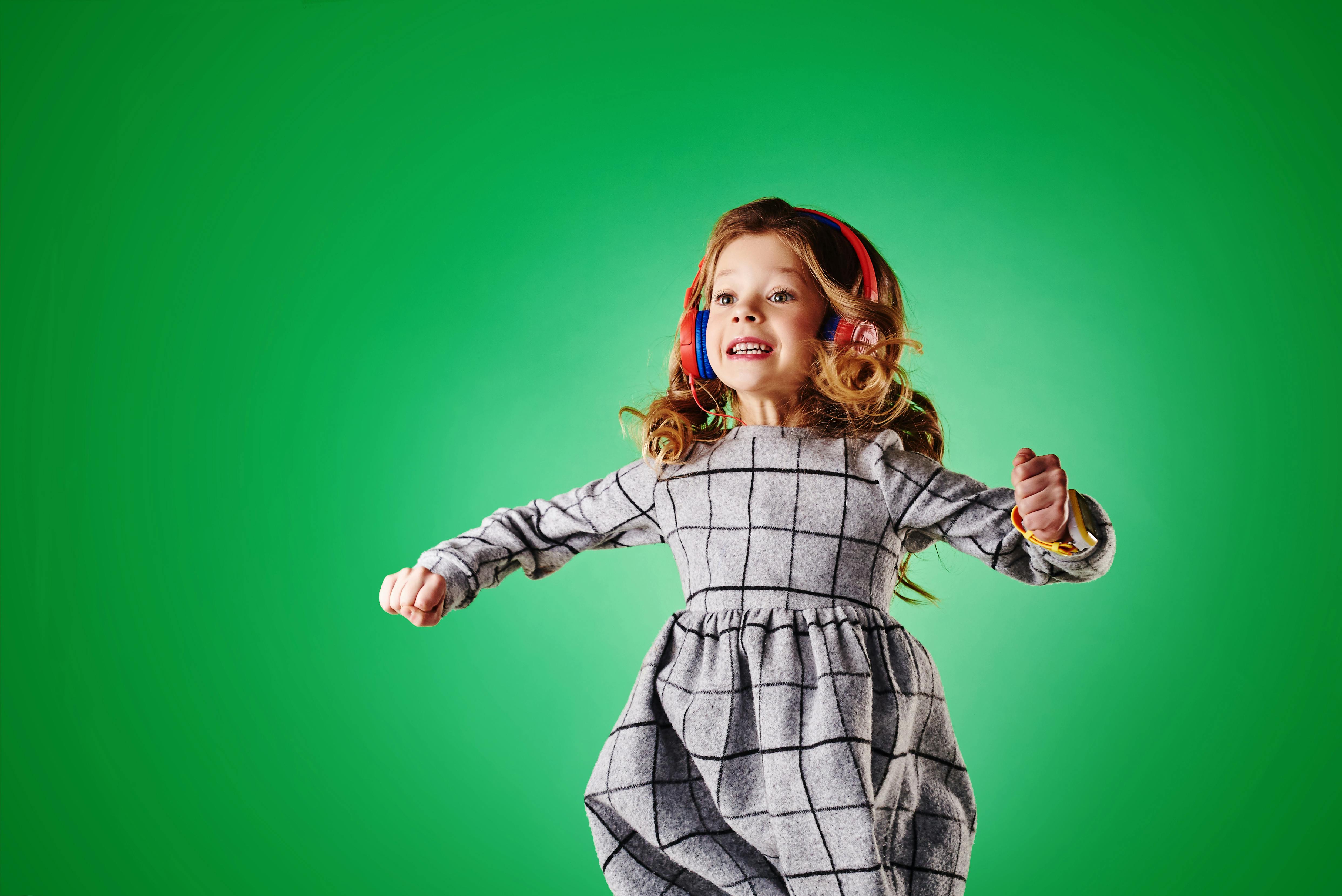 little wearing headphones jumping in front of a green screen