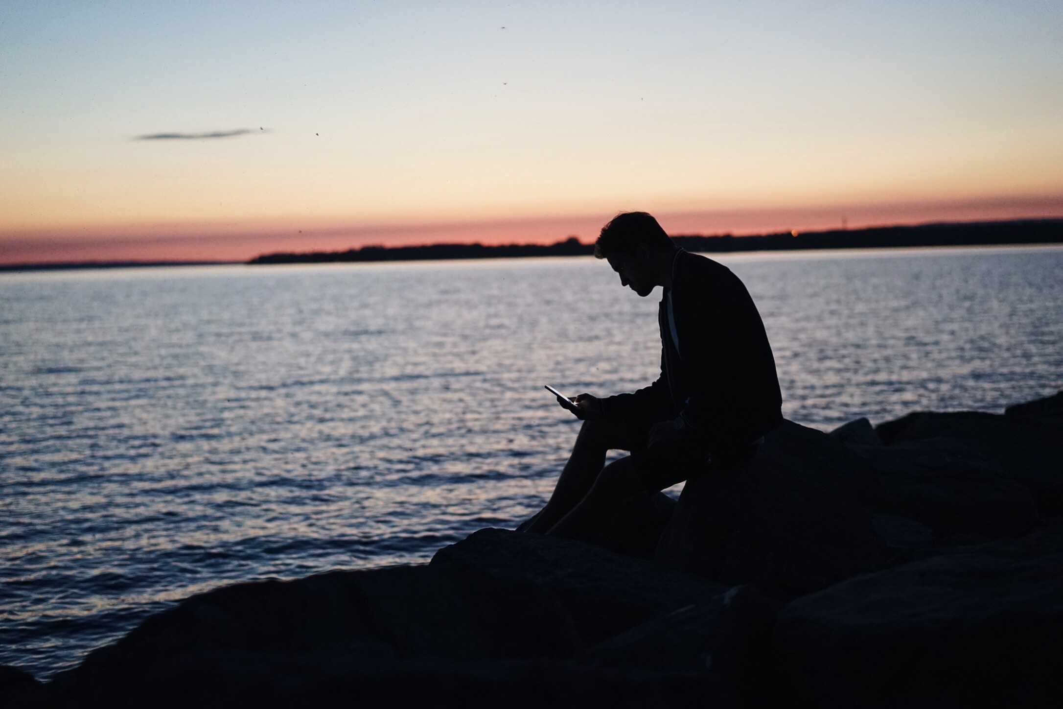 man silhouette seat beside sea