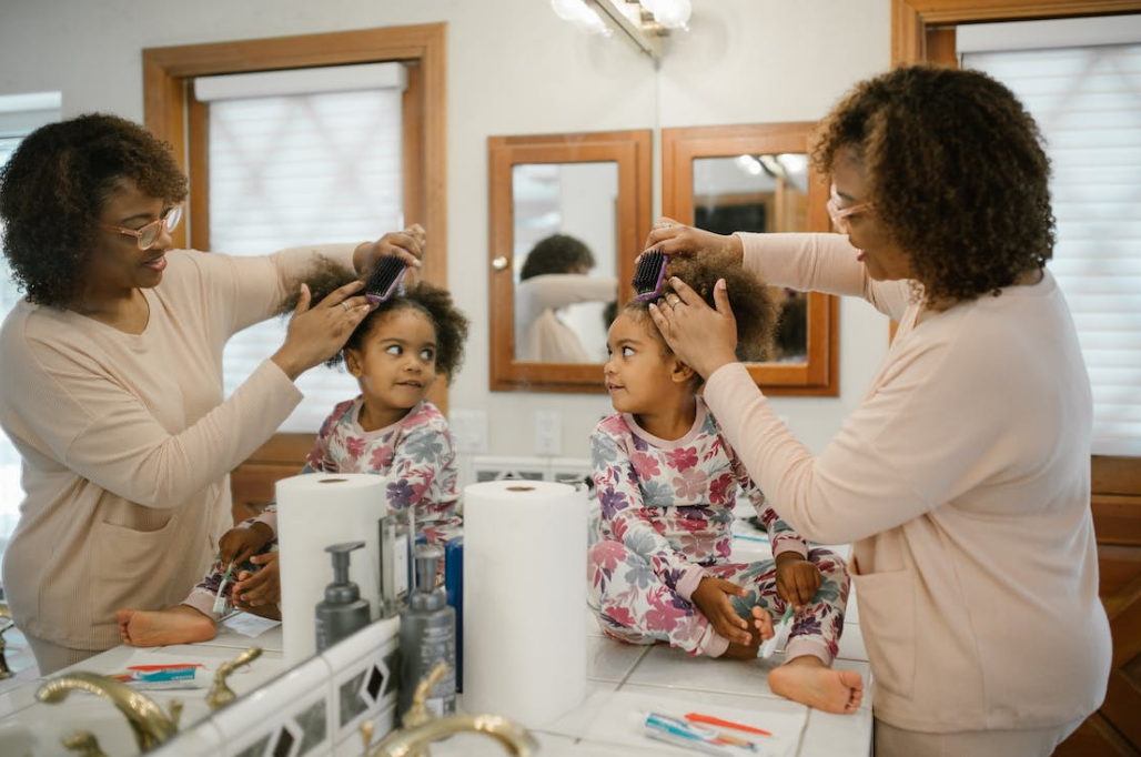 a mirror reflection photoshoot of a black mom combing her daughter's hair