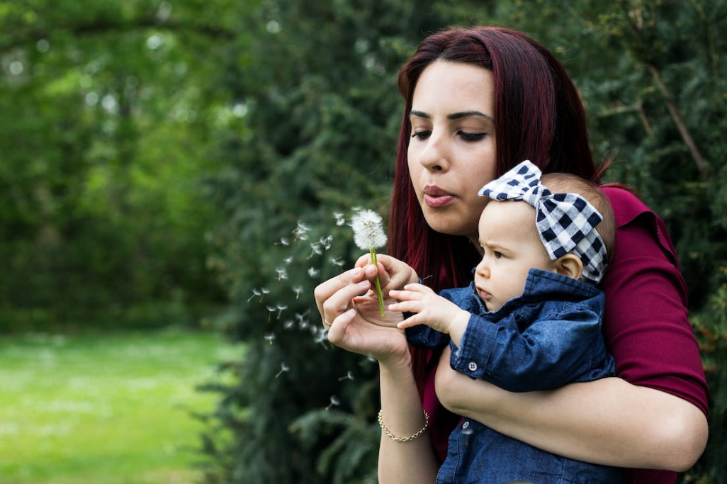 female holding her baby blowing dandelion outdoors