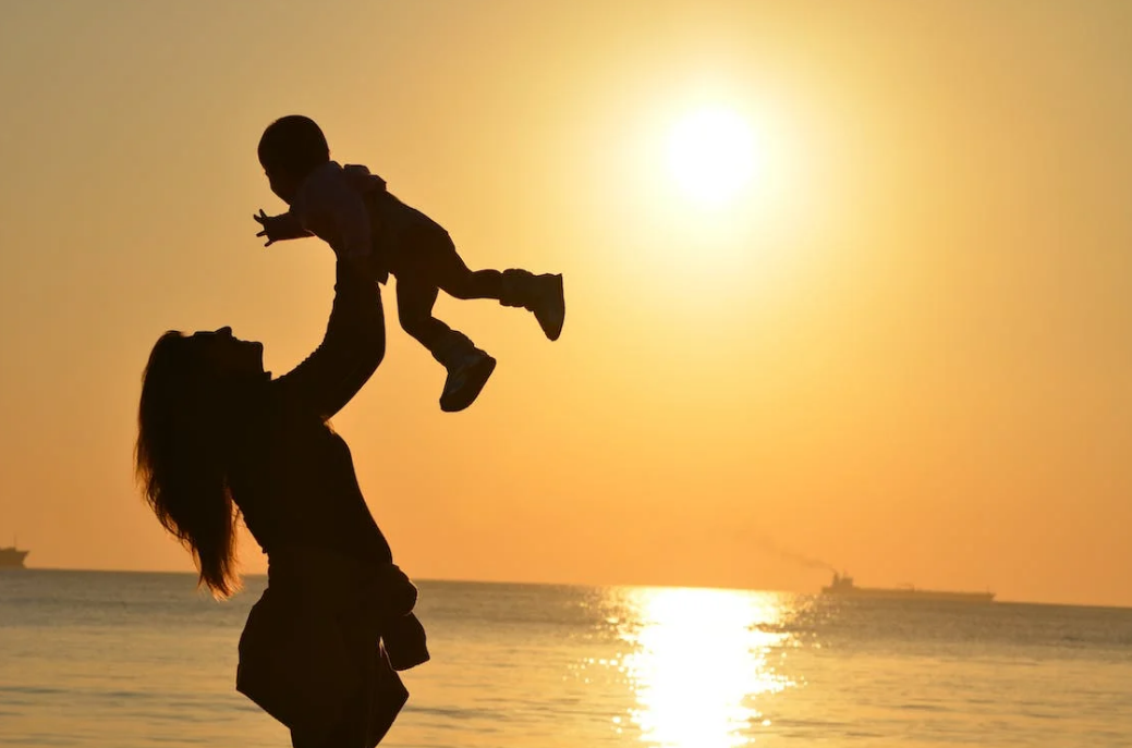 silhouette photos of a female holding her baby high on the beaches