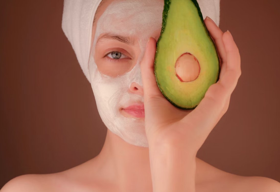 a woman wears a mask pack and holds a avocado