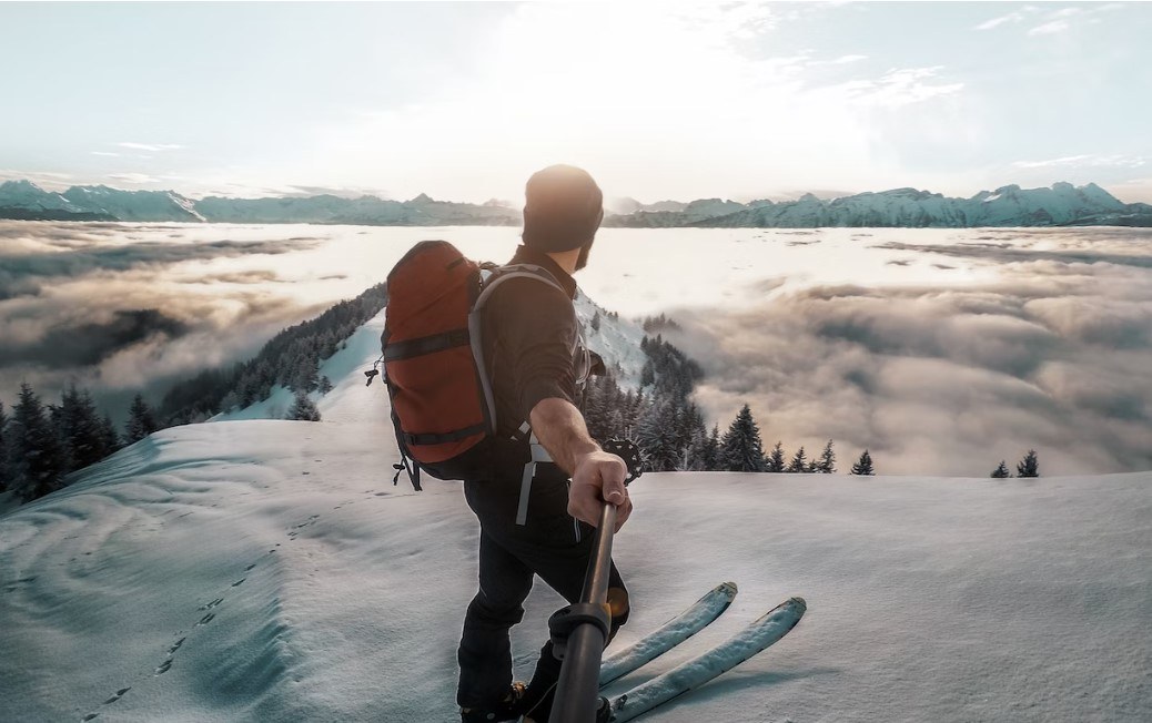 man takes selfie with sunrise on the top of a snow mountain.