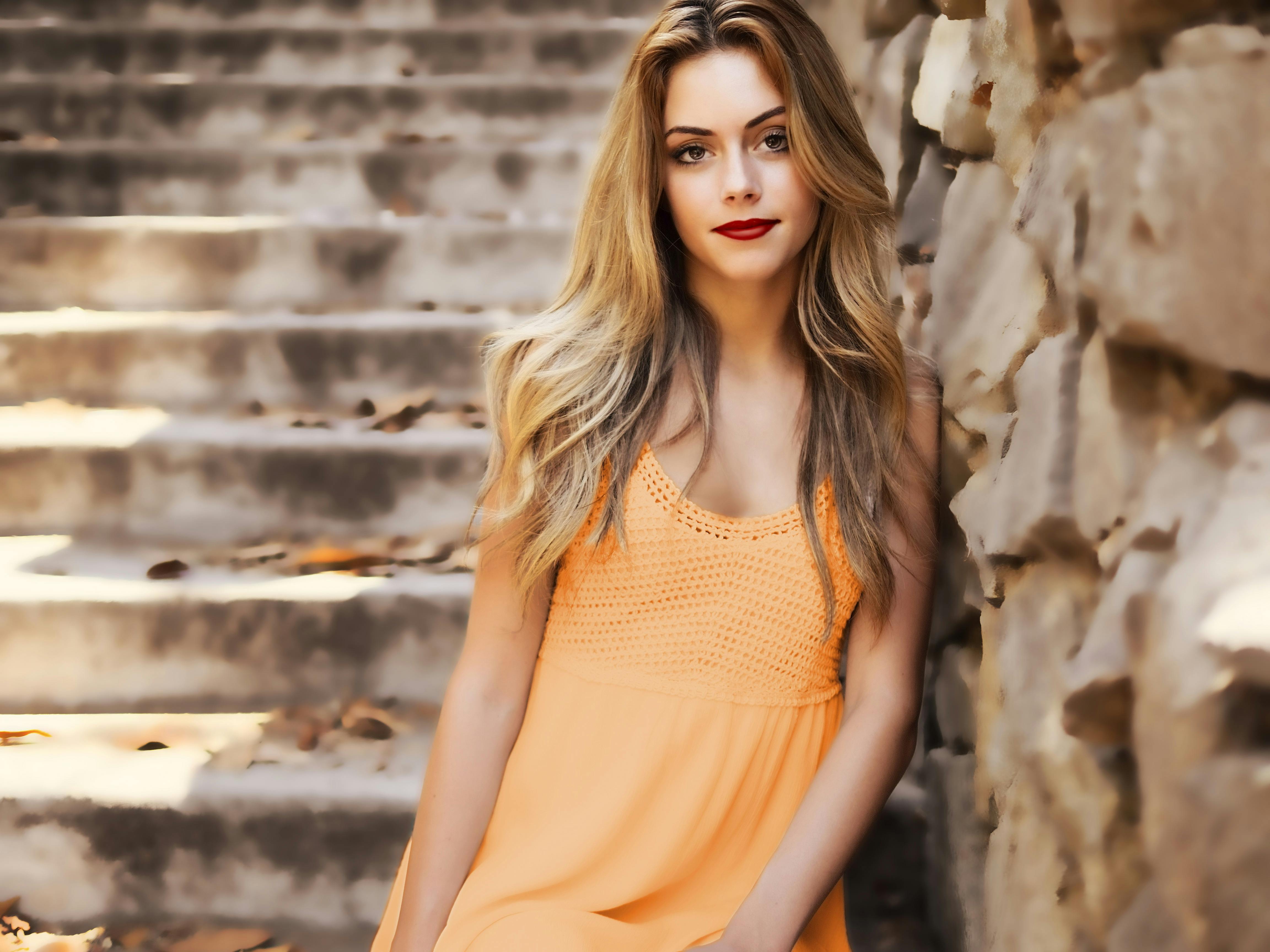 woman with orange colored dress leaning on the wall