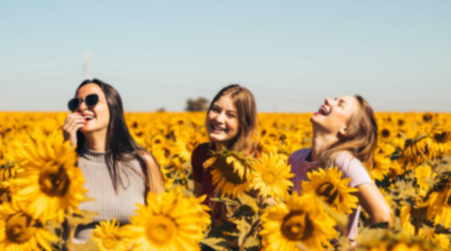 A small blurry photo of three women sanding on a sunflower field