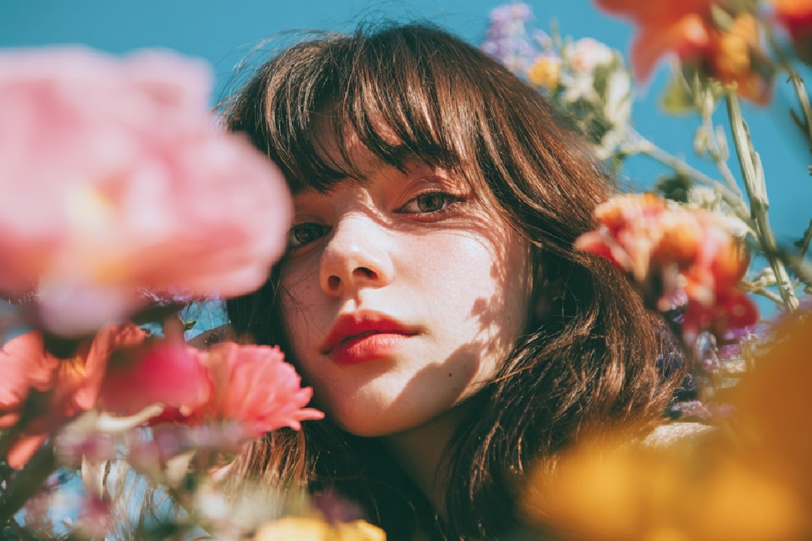 Before image featuring a young woman gazes through vibrant flowers