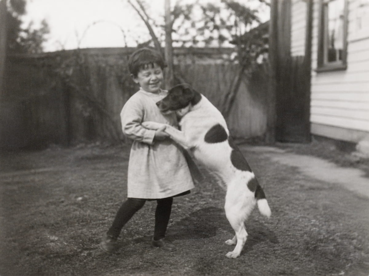 A blurry low quality vintage monochrome candid photo of a child playing with a dog in the backyard