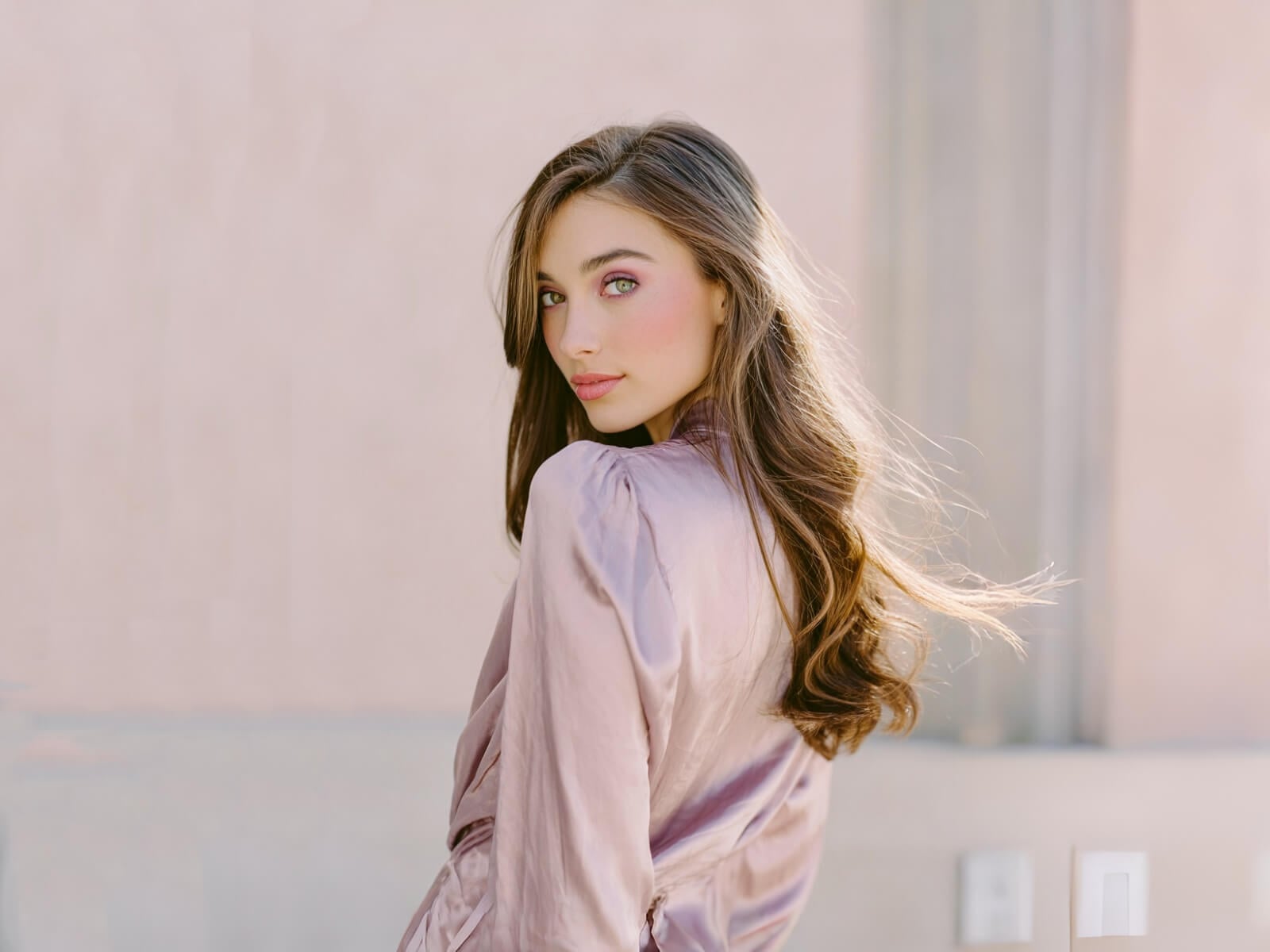 A girl with long hair in pink blouse standing in front of a wall