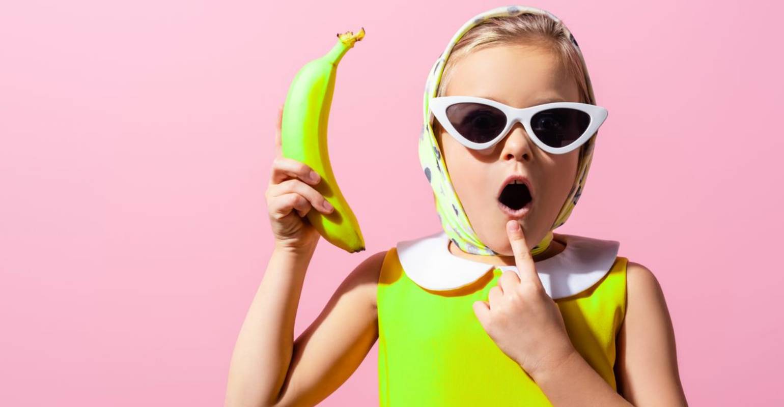 A kid in green outfit holding a banana