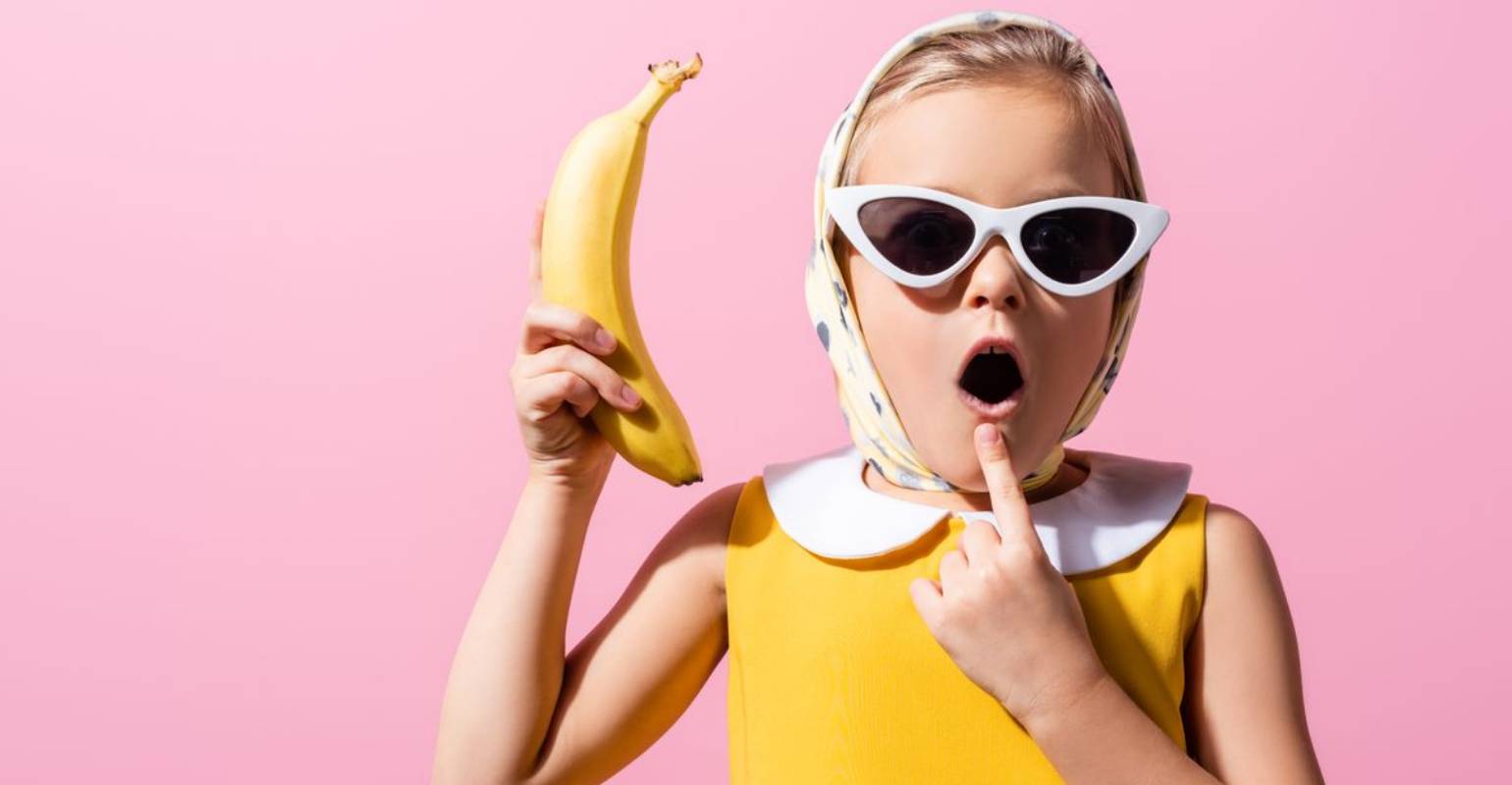 A kid in yellow outfit holding a banana