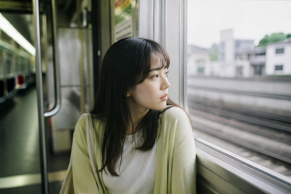 電車に座る女性一人が窓の外を望んでいる